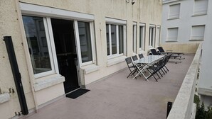 A building with a covered outdoor area featuring a table and chairs, a door, and windows.