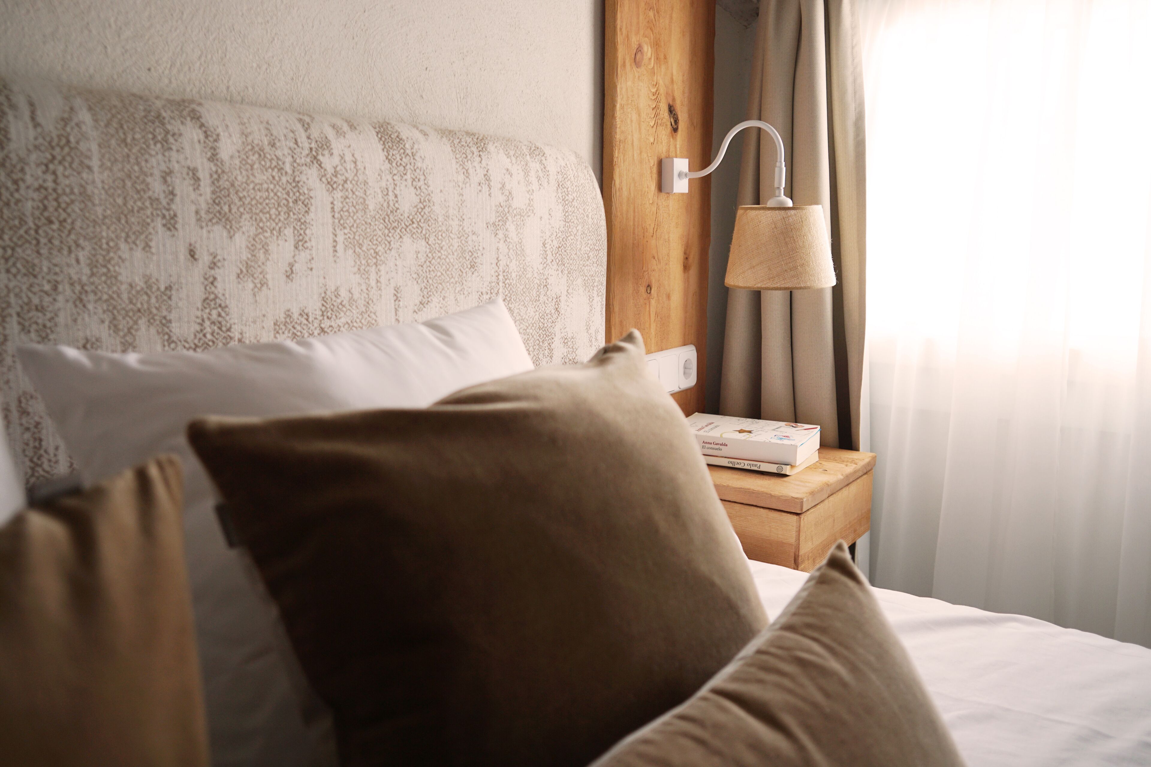 A neatly made bed with pillows, a bedside lamp, and a book on a wooden nightstand.