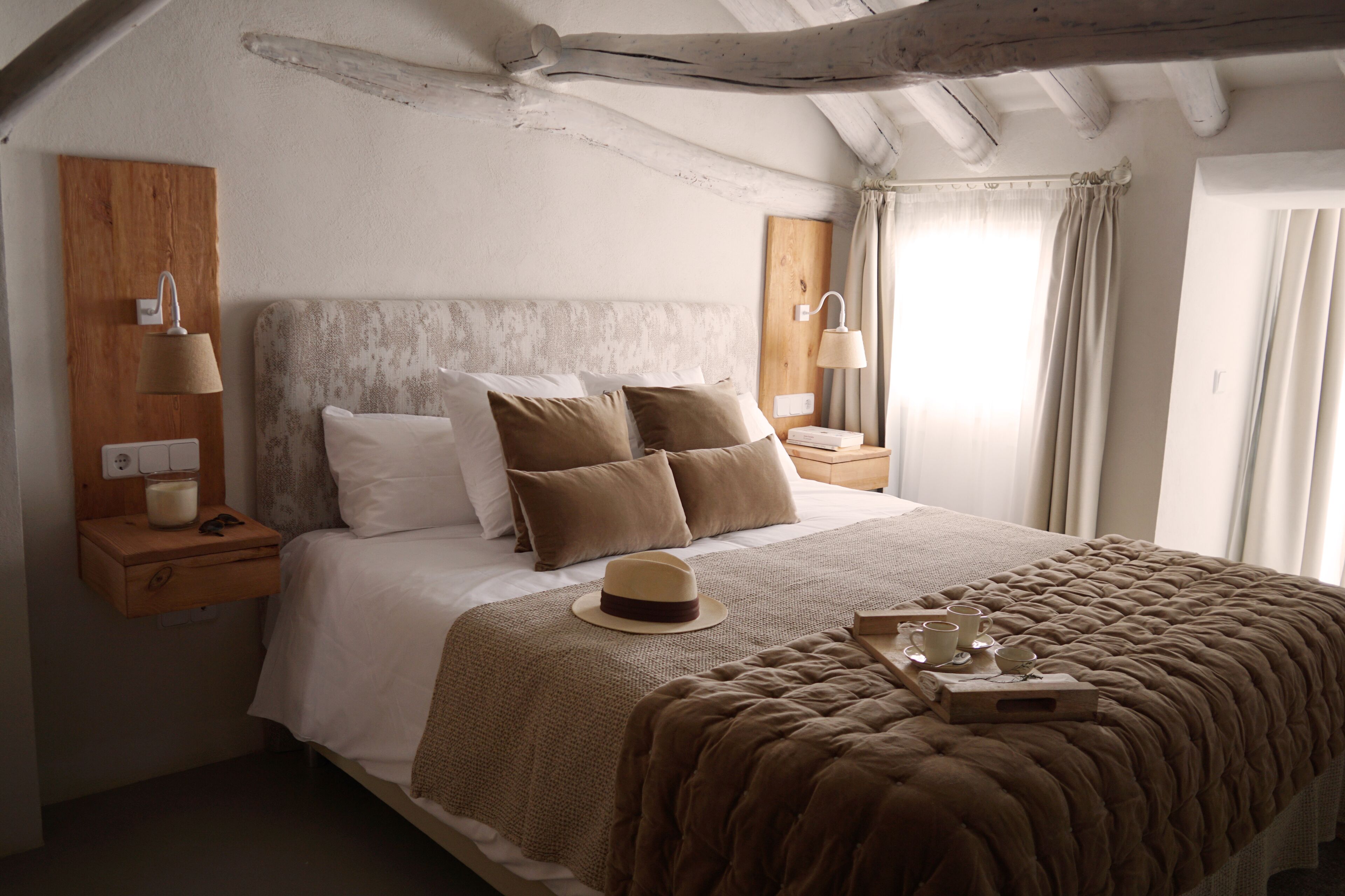 A bedroom with a large bed, wooden headboard, bedside tables with lamps, and a window with curtains.