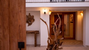 Une sculpture en bois dans un hall d’entrée, avec un banc et une porte donnant sur une pièce.
