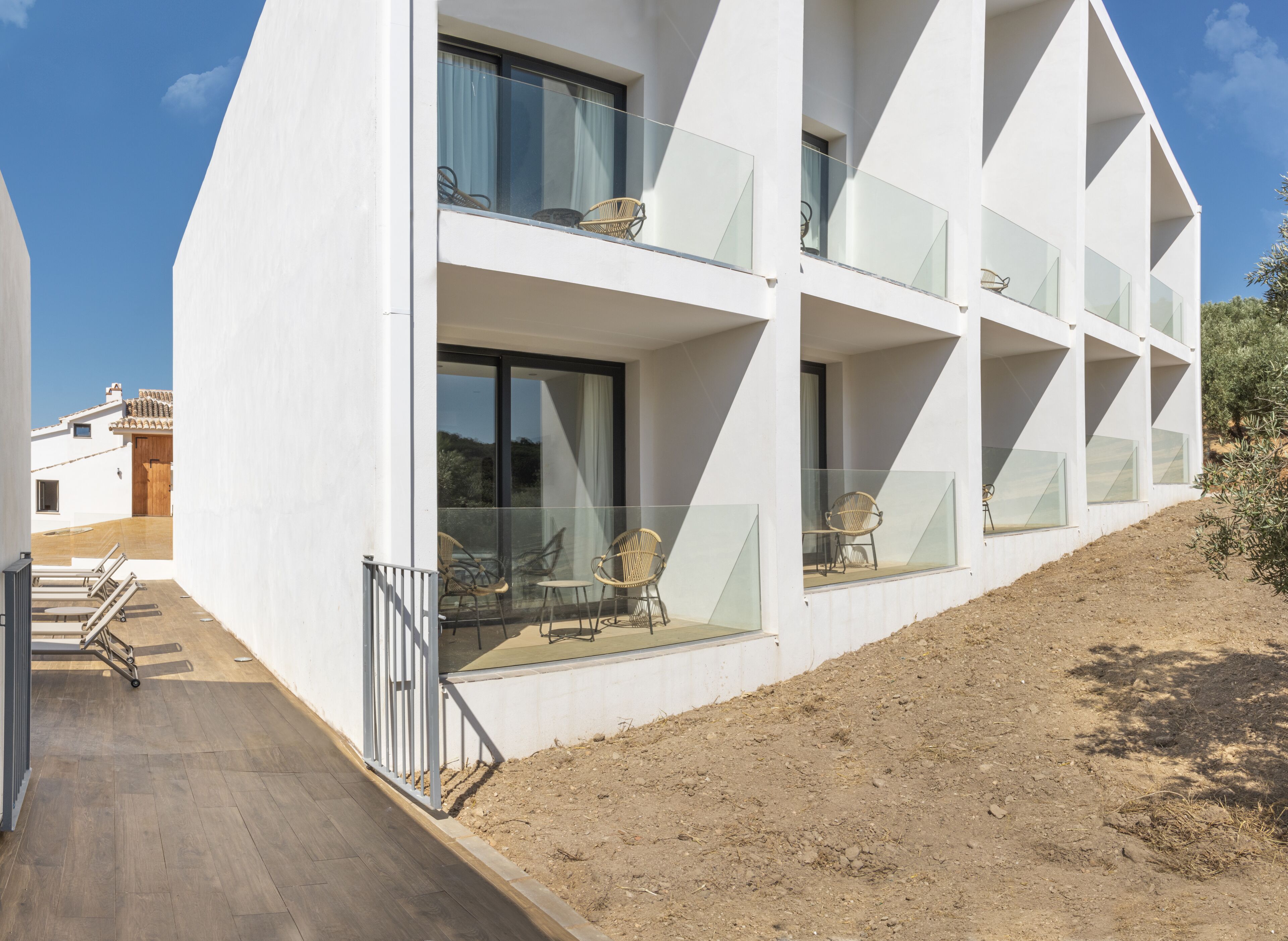 Un edificio moderno de varios pisos con amplios ventanales y balcones, piso de madera y mobiliario para exteriores.