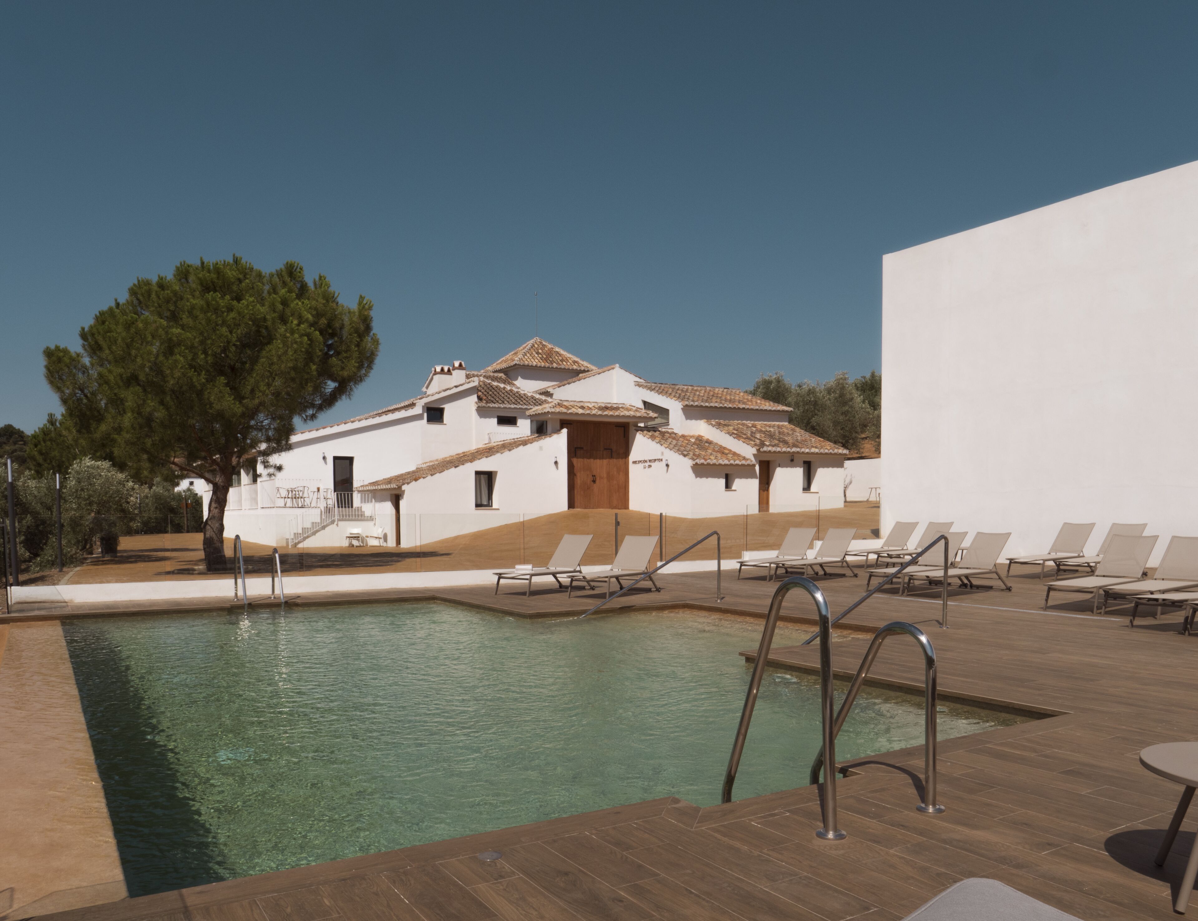 A pool area with lounge chairs and a building with a tiled roof.