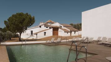 A pool area with lounge chairs and a building with a tiled roof.