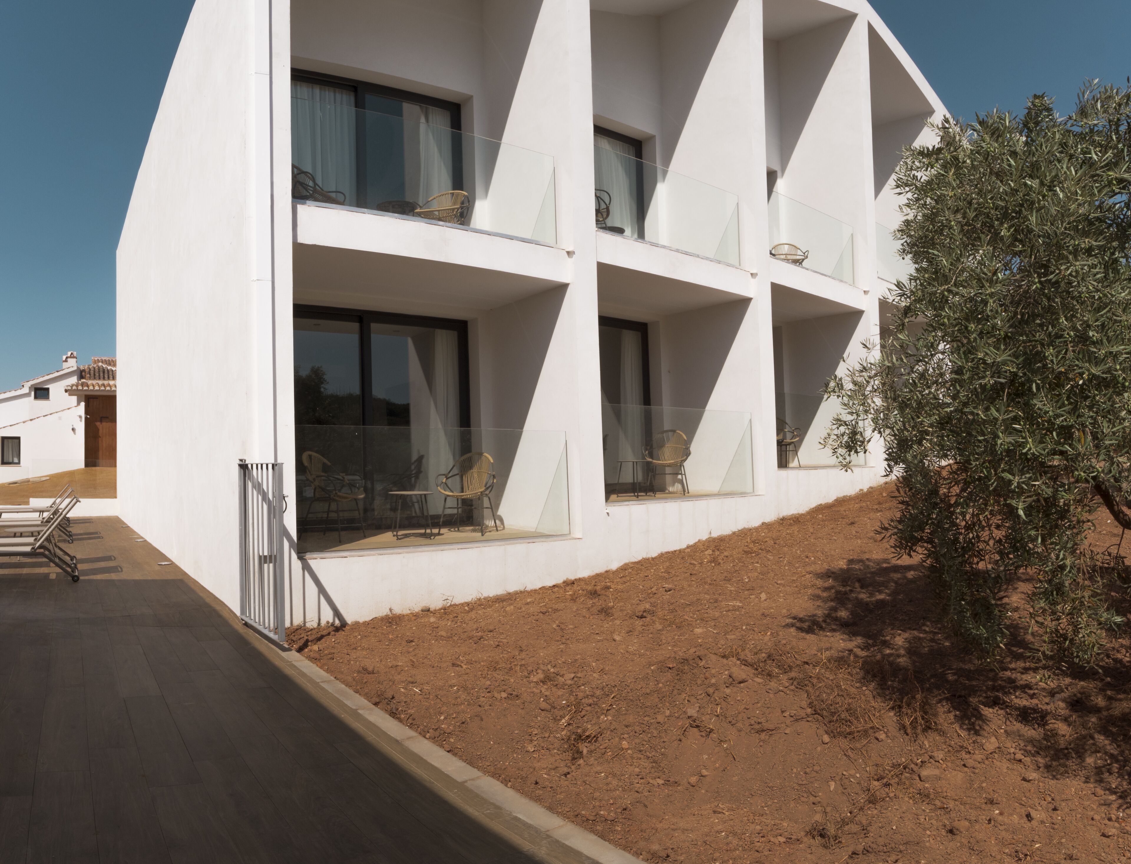 A modern white building with multiple balconies, each with glass railings and wicker furniture.