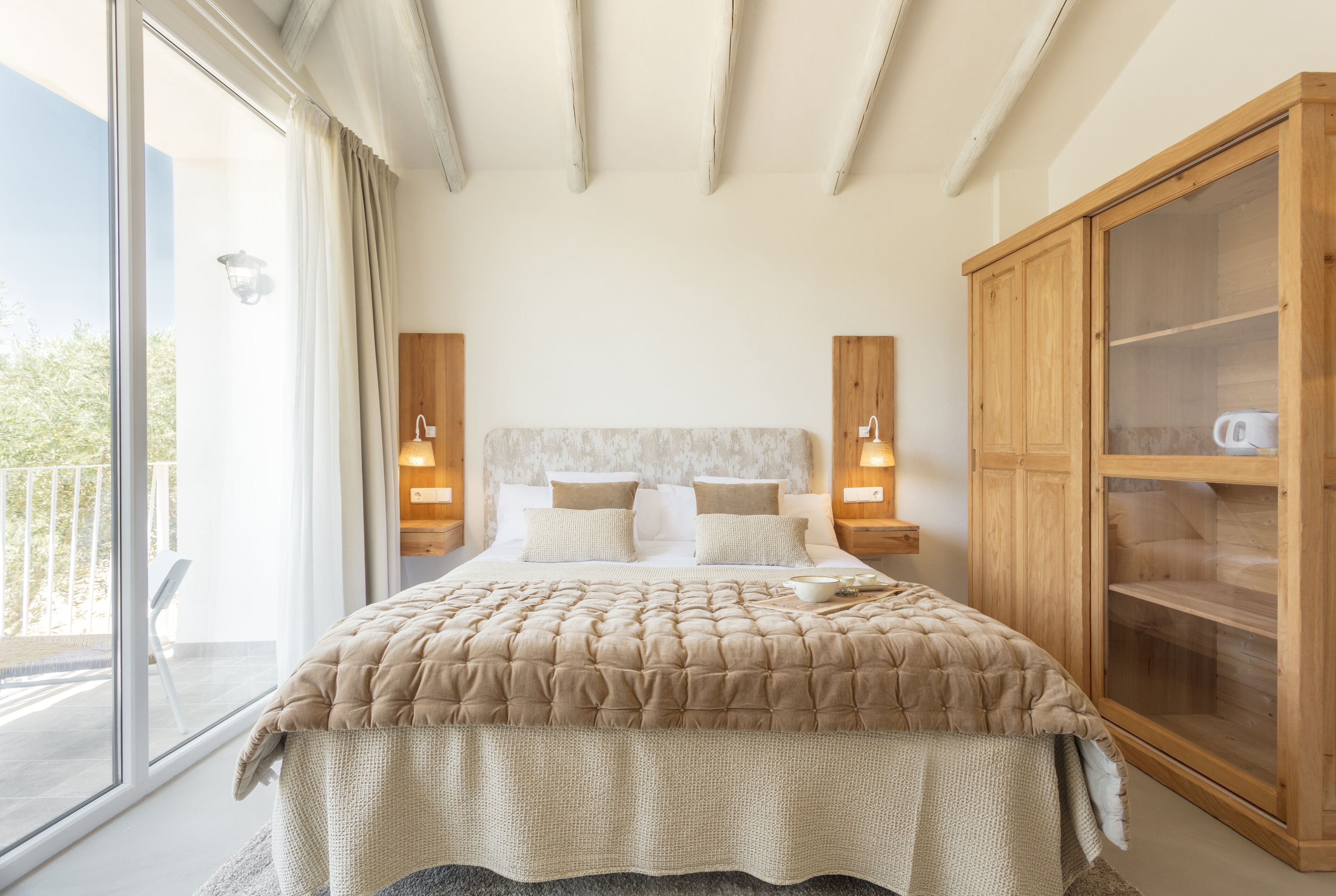 A bedroom with a large bed, a wooden wardrobe, and a balcony with a view.