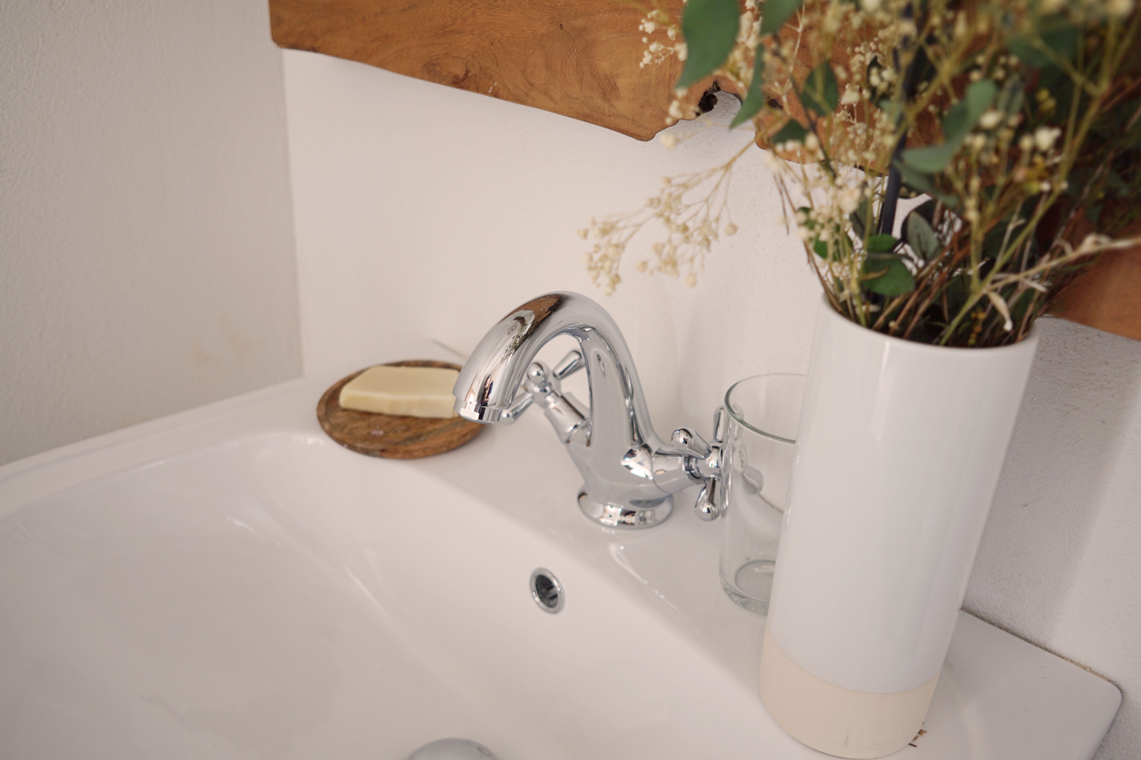 A white bathroom sink with a chrome faucet, a glass, and a vase with flowers.