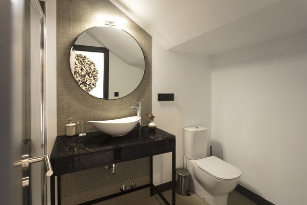 Un baño moderno con un espejo redondo, un lavabo blanco y un inodoro.