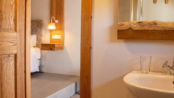 Una puerta de madera que da a un dormitorio con una cama, una mesita de noche y una lámpara fijada a la pared.