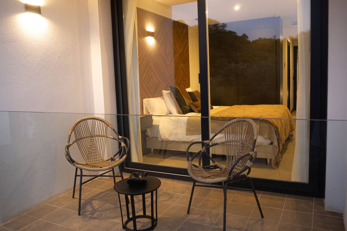 Un balcon avec deux fauteuils en osier, une petite table et une paroi en verre.