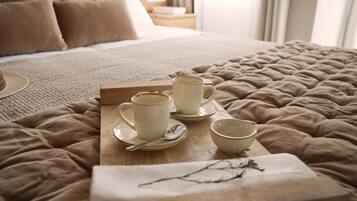 A neatly made bed with a beige quilt, a tray with three cups and a spoon, and a branch on a napkin.