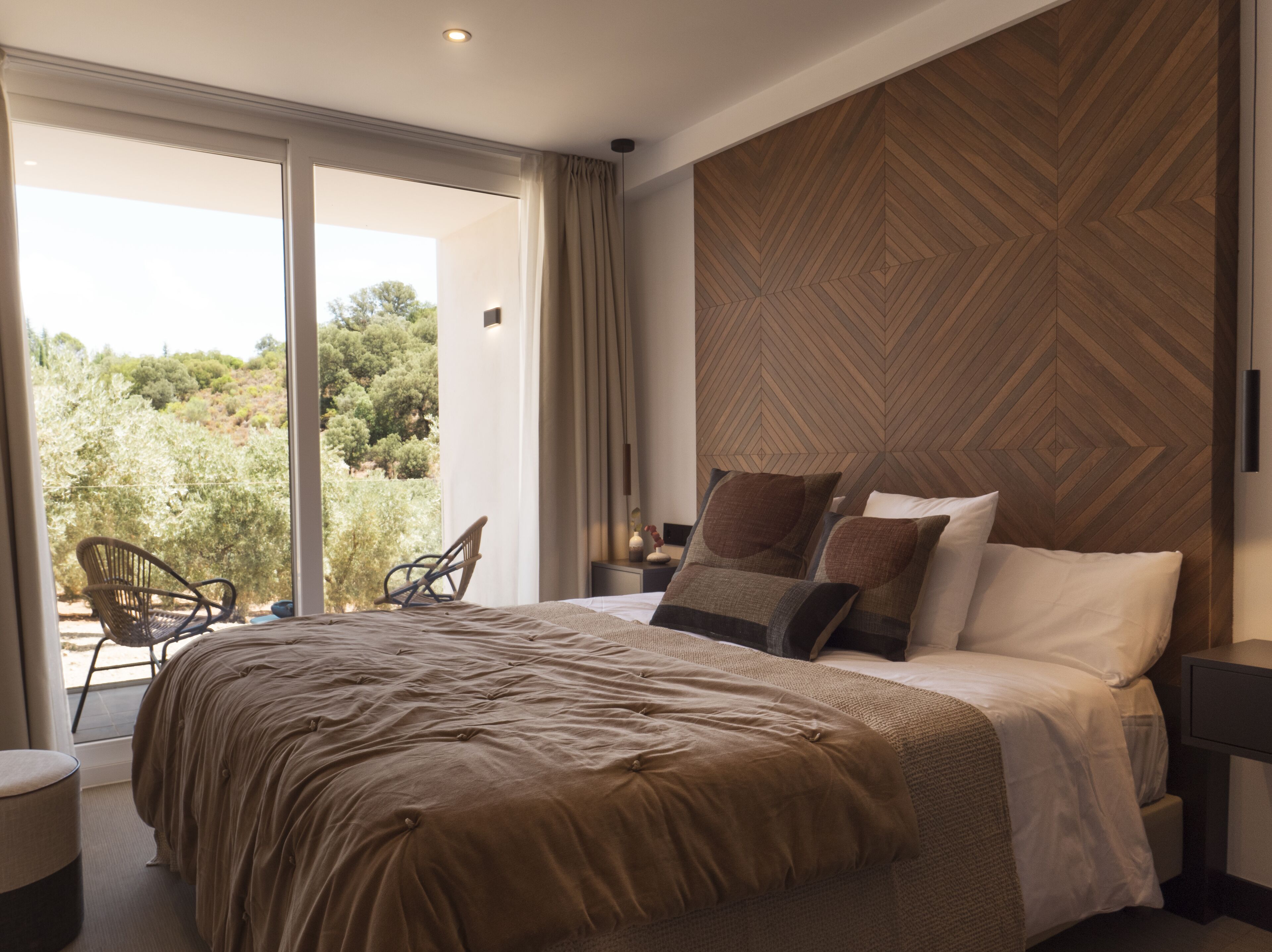 Une chambre avec un grand lit, une vue sur la verdure et un motif décoratif en bois sur un des murs.