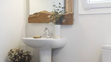 Un bagno con un lavandino bianco, uno specchio con cornice in legno e un piccolo sgabello di legno.