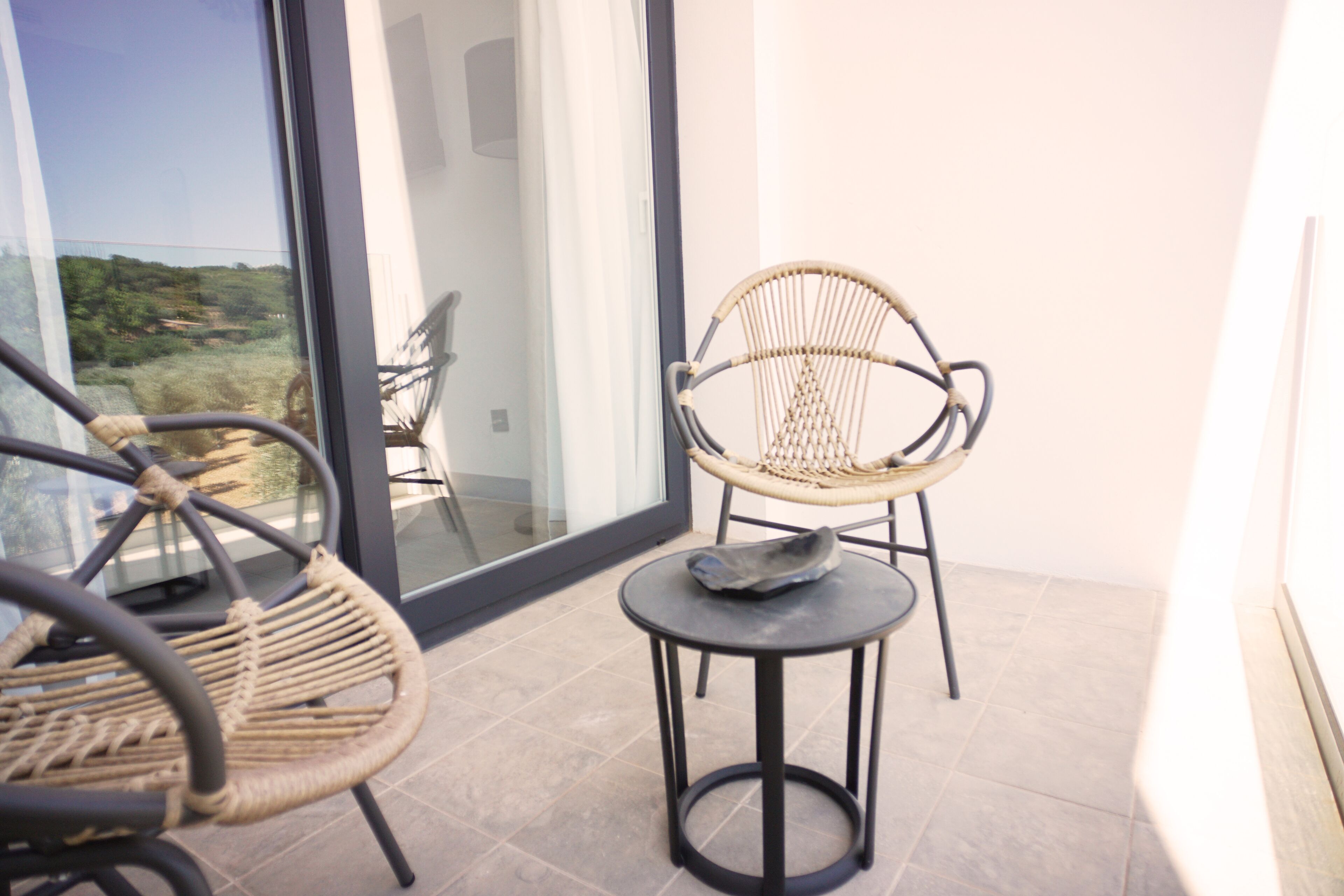 Un balcon agrémenté de fauteuils en osier et d’une petite table, offrant une vue sur un paysage pittoresque.