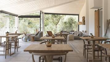 Comedor de concepto abierto con mesas y sillas de madera, un sofá y vistas al exterior.