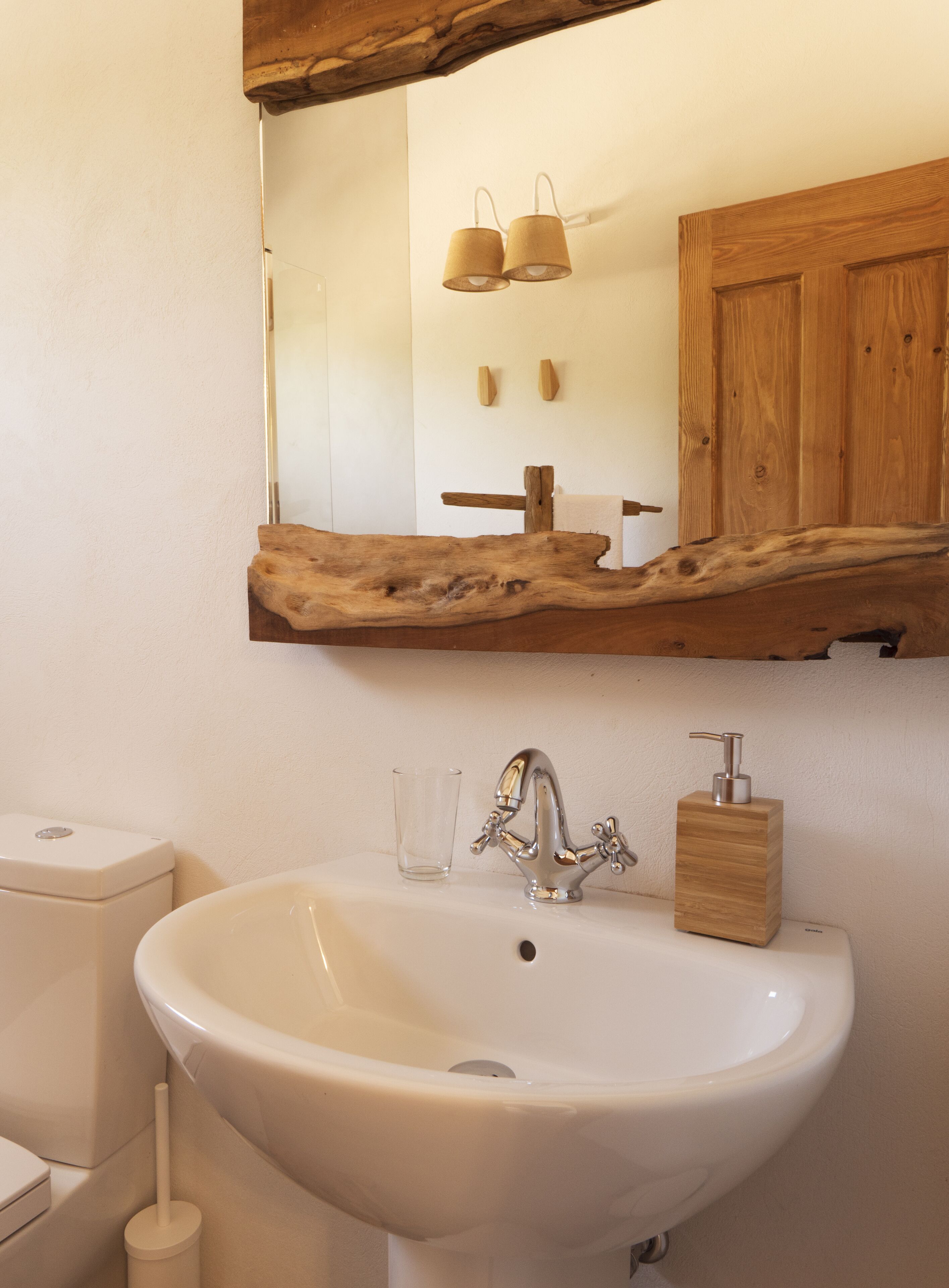 A bathroom with a wooden vanity, a white sink, a mirror, and a wooden shelf above the mirror.