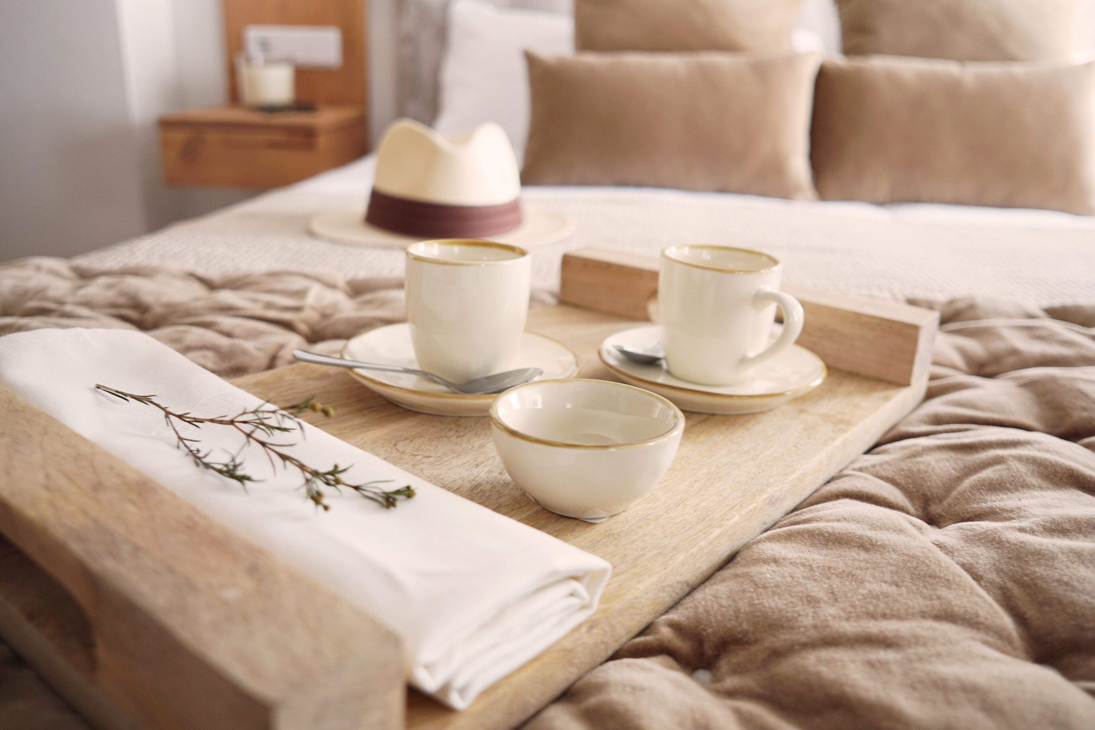 A neatly arranged breakfast tray on a bed with a folded towel and a sprig of thyme.