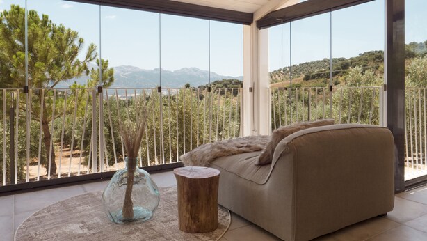 Un balcon avec un canapé, un vase en verre et un tabouret en bois.