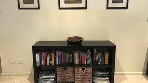Una stanza con una libreria contenente libri e riviste, una ciotola decorativa sopra e tre quadri appesi al muro.