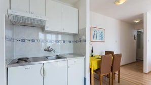 A compact kitchen with white cabinets, a built-in stove, and a sink. There is a dining area with a yellow table and chairs.