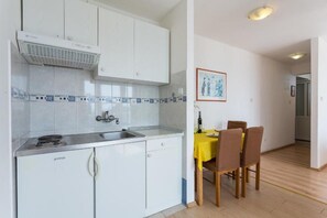 A compact kitchen with white cabinets, a built-in stove, and a sink. There is a dining area with a yellow table and chairs. - Charming Studio Apartment With Beautiful Panoramic sea View (Dubrovnik)