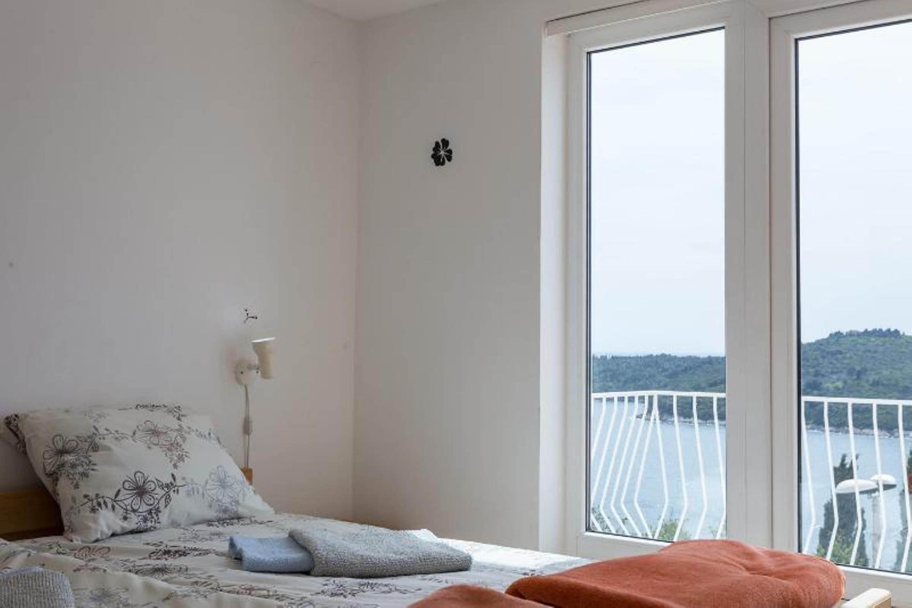 A bedroom with a bed, a window with a view of a balcony, and a wall-mounted light.