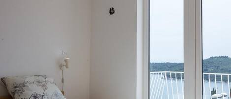 A bedroom with a bed, a window with a view of a balcony, and a wall-mounted light.