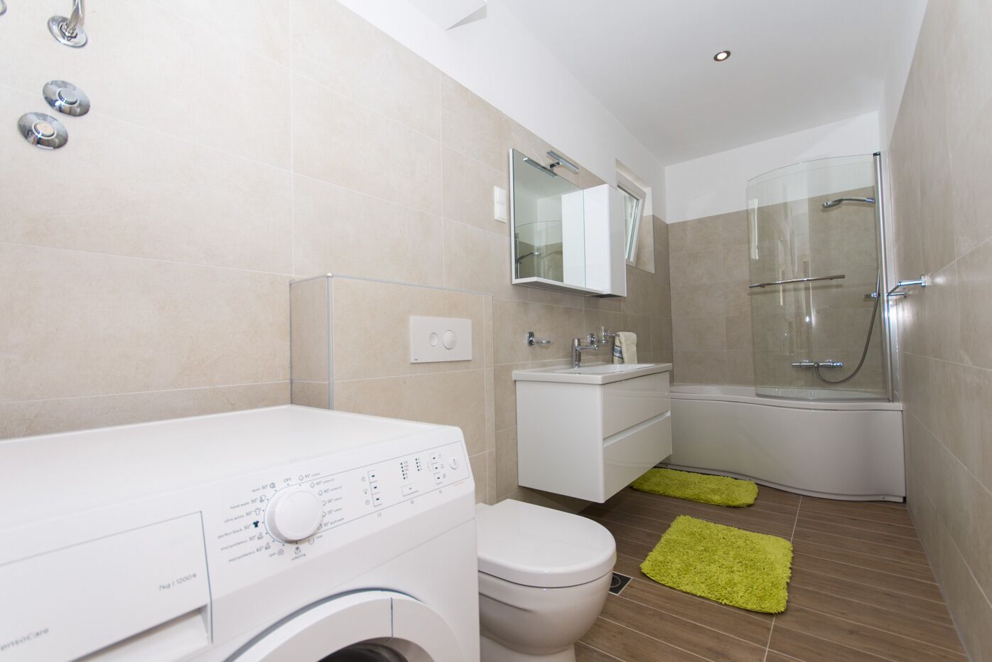 A compact bathroom with a washing machine, toilet, sink, and glass-enclosed shower.