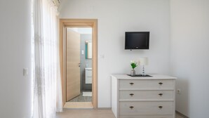 Un dormitorio con cama, cómoda, televisión montada en la pared y baño visible a través de una puerta abierta.