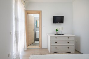 A bedroom with a bed, a dresser, a TV mounted on the wall, and a bathroom visible through an open door.