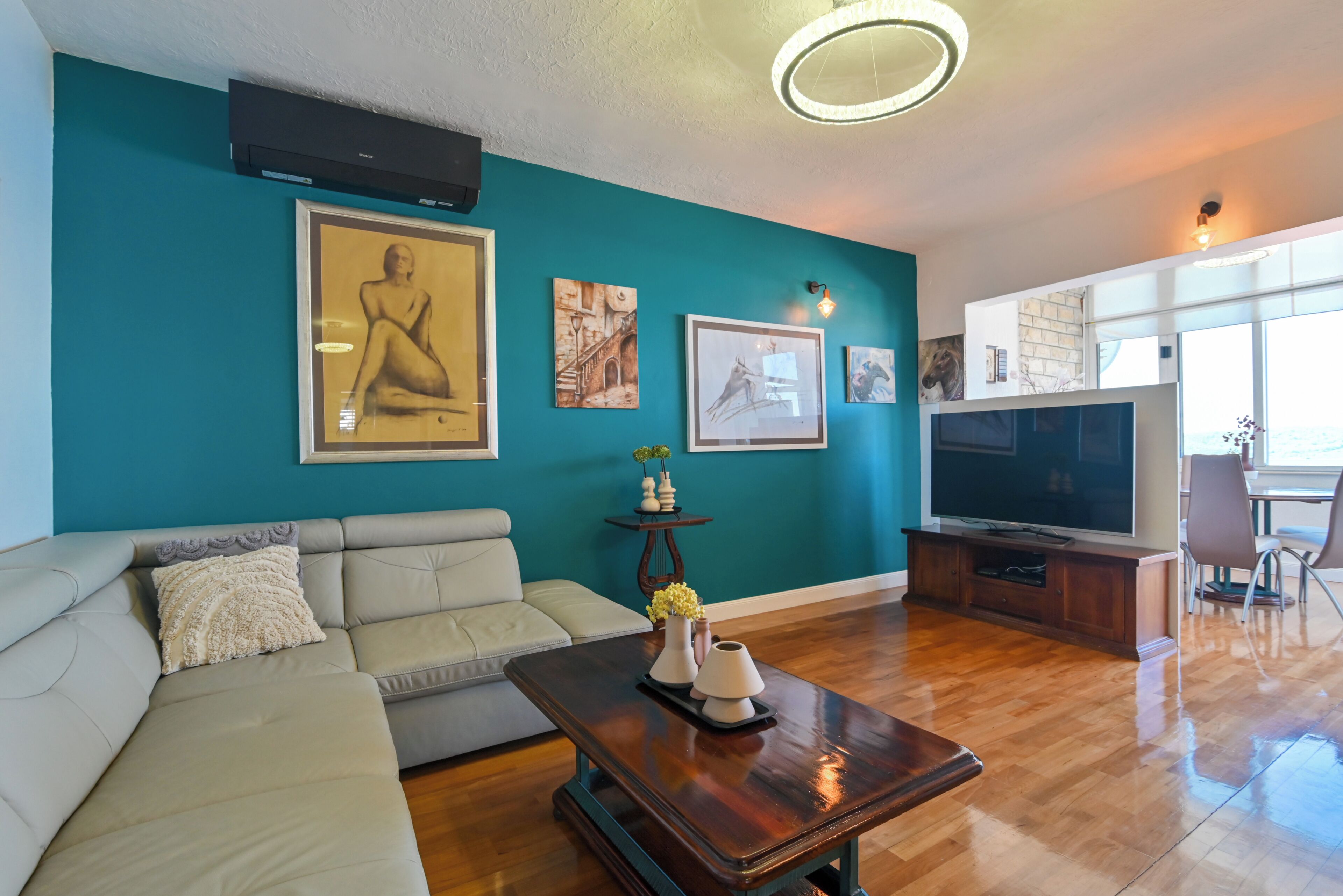 Ett vardagsrum med turkosa väggar, en beige soffa, ett soffbord i trä och en platt-TV.