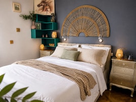 Un dormitorio con una cama, una mesita de noche, un estante en la pared y una obra de arte colgada.