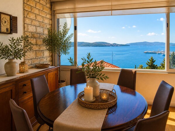 Un espace repas avec vue sur la mer, un mur en pierre et une grande fenêtre.