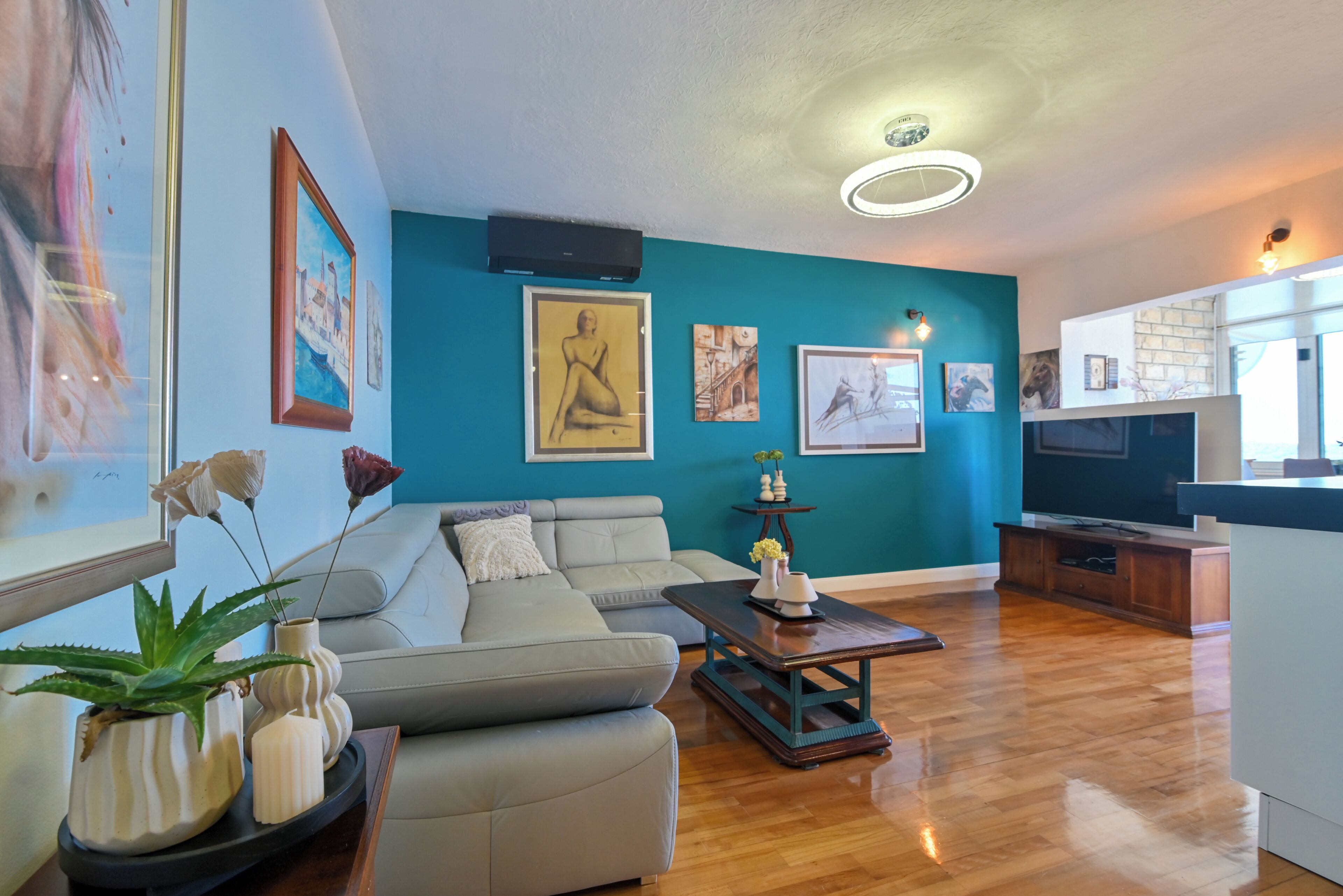 A modern living room with a teal accent wall, a grey sofa, a wooden coffee table, and a flat-screen TV.
