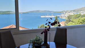 A table with a vase of flowers, a window with a view of a harbor, and a chair. - Apartment With Breathtaking sea View (Trogir)
