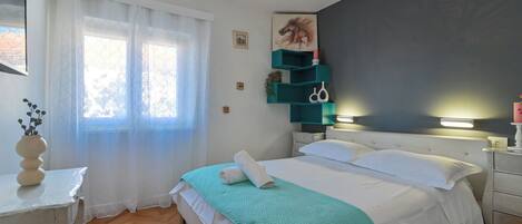 Un dormitorio ordenado con cama, mesita de noche, ventana con cortinas y estante en la pared con objetos decorativos.