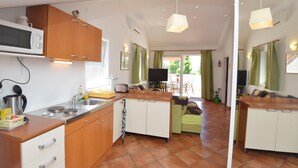 A compact kitchen with a microwave, toaster, and sink. There is a dining area with a table and chairs, and a sofa. The room has a tiled floor and a ceiling with recessed lighting. - Villa Ellys Apartment Ely (Dubrovnik)
