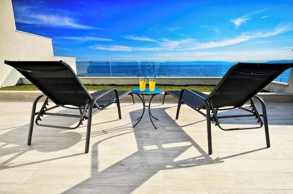 A terrace with two lounge chairs and a table, overlooking a scenic ocean view.
