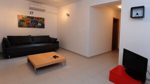 A modern living room with a black sofa, a wooden coffee table, a red entertainment unit, and a flat-screen TV. - Citybreak Apartman With Private Beach Near Split (Omis)