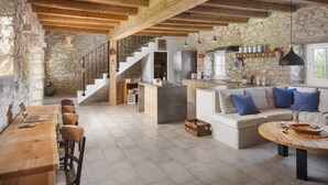 A spacious living area with a wooden dining table, a sofa with blue cushions, and a kitchen area with stone walls and wooden beams. - Villa Flavia - Stunning Villa in Istria, Croatia (Umag)