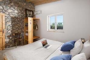 A bedroom with a stone wall, wooden furniture, a bed with blue and white pillows, a laptop on the bed, and a window with a view. - Villa Flavia - Stunning Villa in Istria, Croatia (Umag)