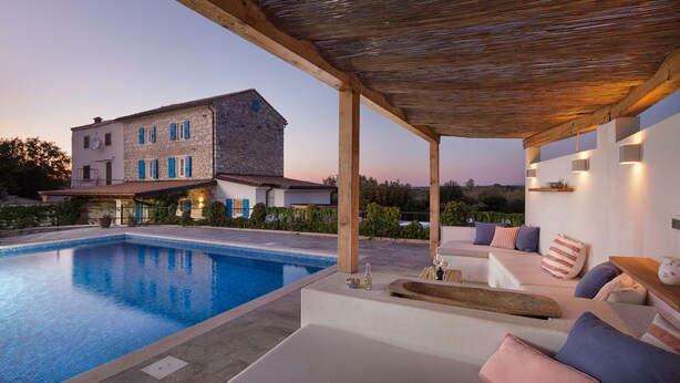 A poolside area with a stone building in the background, a covered seating area with cushions, and a clear view of the pool. - Villa Flavia - Stunning Villa in Istria, Croatia (Umag)