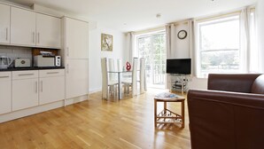 Een moderne keuken met witte kasten en een eethoek met een glazen tafel en stoelen.