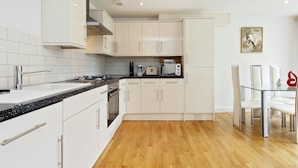 Een moderne keuken met witte kasten, een zwart aanrecht, roestvrijstalen apparatuur, en een eethoek met een glazen tafel en stoelen.