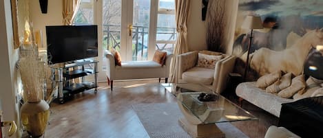 A spacious living room with a large window, a flat-screen TV, a sofa, a chair, and a coffee table.