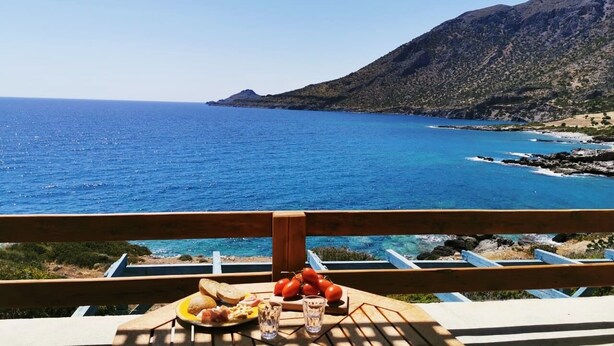 A table with food and drinks, overlooking a coastal view with a mountain in the background. - Nefeli's traditional suite no.12 (Gortyna)