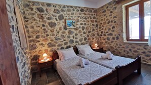 A room with two beds, stone walls, a window, and a painting. - Nefeli's traditional suite no.12 (Gortyna)