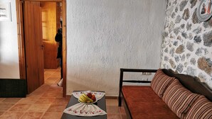 A room with a wooden door, a stone wall, a sofa, and a table with fruit. - Nefeli's traditional suite no.12 (Gortyna)