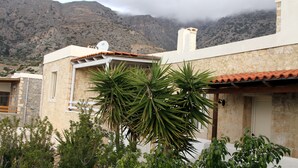 A building with a stone facade, a tiled roof, and a mountain backdrop. - Nefeli's traditional suite no.12 (Gortyna)