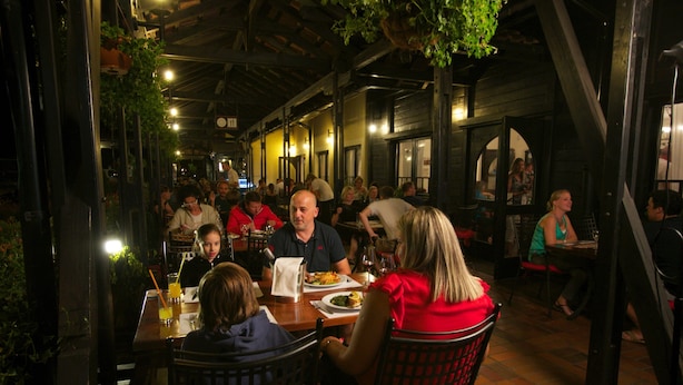 Un restaurante con terraza, vigas de madera y plantas colgantes.