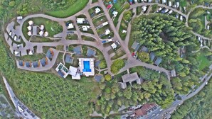 Vista aérea de un camping con vehículos recreativos, una piscina y varios edificios rodeados de árboles frondosos.